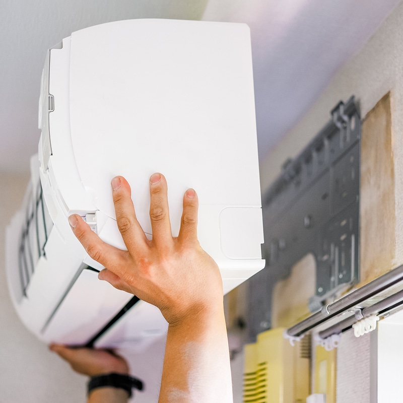 Main d'une personne fixant une unité intérieure de climatisation murale blanche sur son support pour installation.