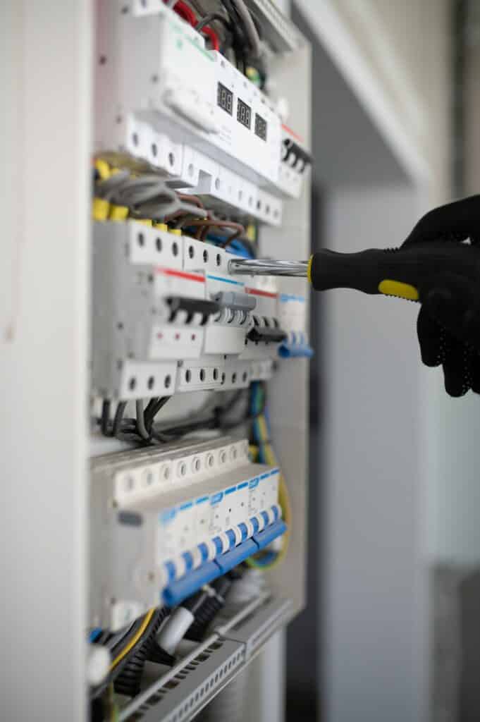 Main gantée ajuste un disjoncteur d'un tableau électrique avec un tournevis. Fils, modules et afficheur numérique "8.8.8 V" d'installation moderne.