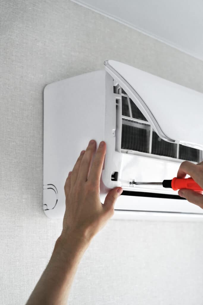 Mains d'un technicien ouvrant un climatiseur mural blanc avec un tournevis pour son entretien ou sa réparation.
