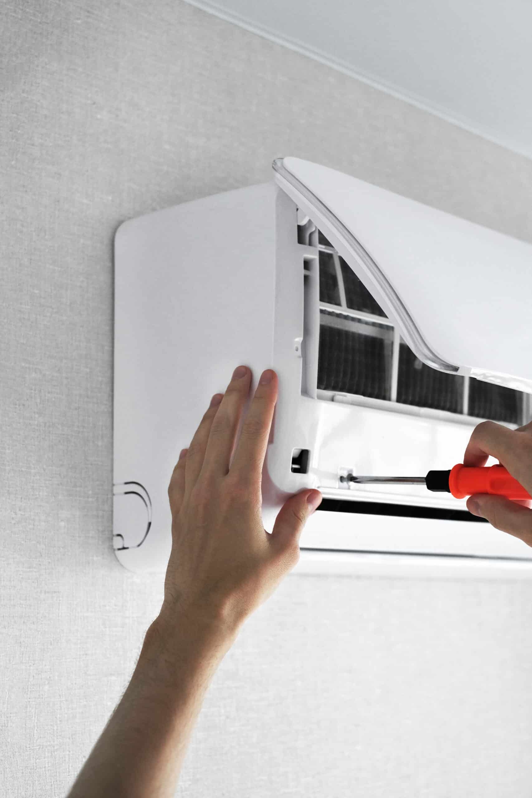 Mains d'un technicien ouvrant un climatiseur mural blanc avec un tournevis pour son entretien ou sa réparation.
